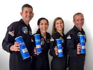 four people in blue flight suits hold blue paper cylinders up for a portrait