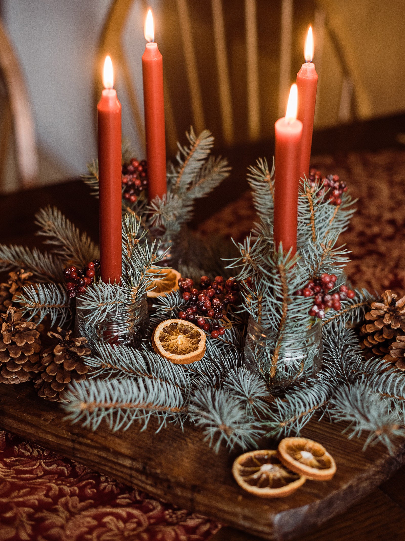 Table centerpiece with pinecones, foliages, berries, dried citrus fruit slices, and candles.