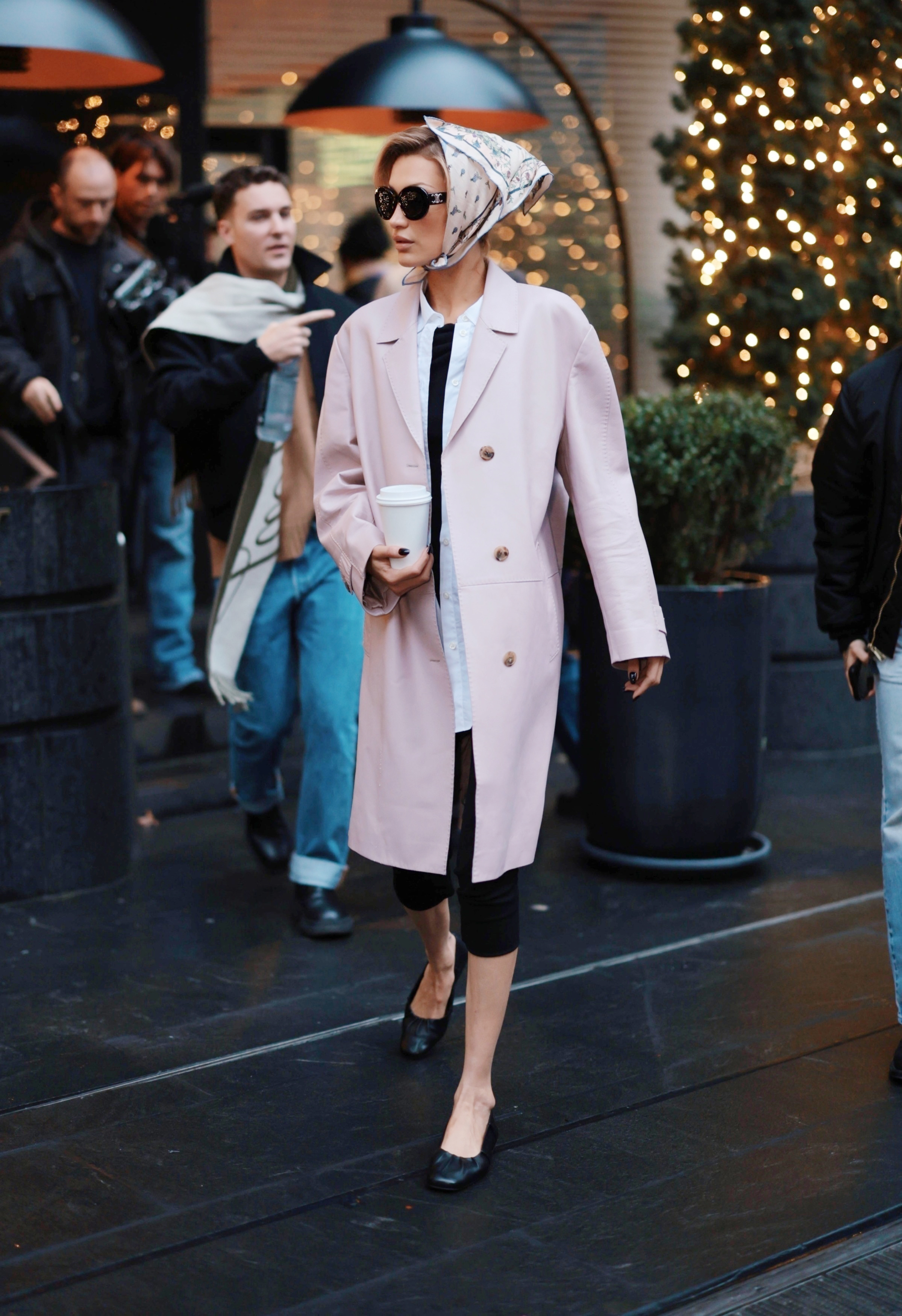 Bella Hadid wears a head scarf, pink coat, black capri pants, and black ballet flats.