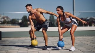 man and woman outdoors during kettlebell workout holding a kettlebell in one hand in squat position