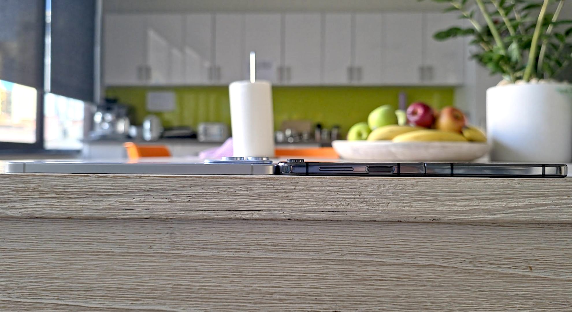 Two phones face down on a table in front of a bowl of fruit