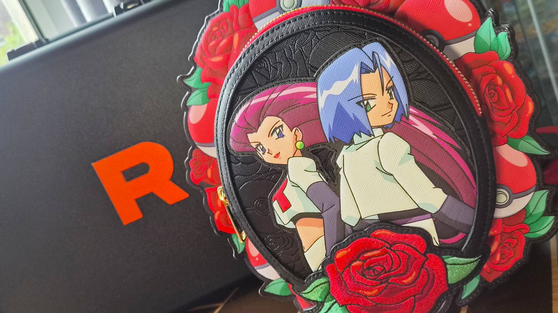Image of the Team Rocket Cameo Mini Backpack sitting in front of a Team Rocket suitcase.