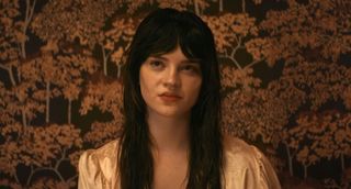 Elle sitting against backdrop of trees with yellow leaves in Her Private Hell