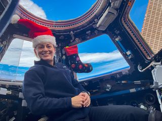NASA astronaut Nicole Mann, wearing a Santa hat, poses in front of the International Space Station cupola.