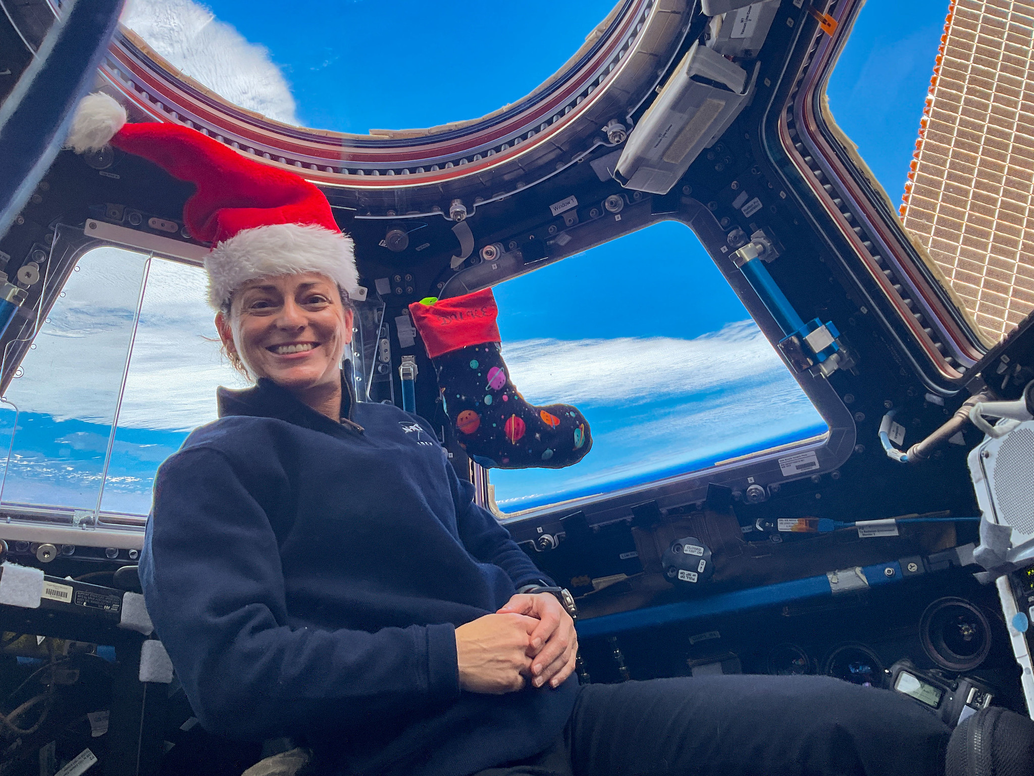 NASA astronaut Nicole Mann, wearing a Santa hat, poses in front of the dome of the International Space Station.