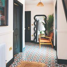 A hallway with a patterned tiled floor, a dado rail on the walls and black skirting boards and doors
