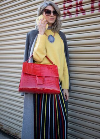 Samantha Angelo dressed in a yellow knitted jumper, grey coat, striped trousers and bright red bag.