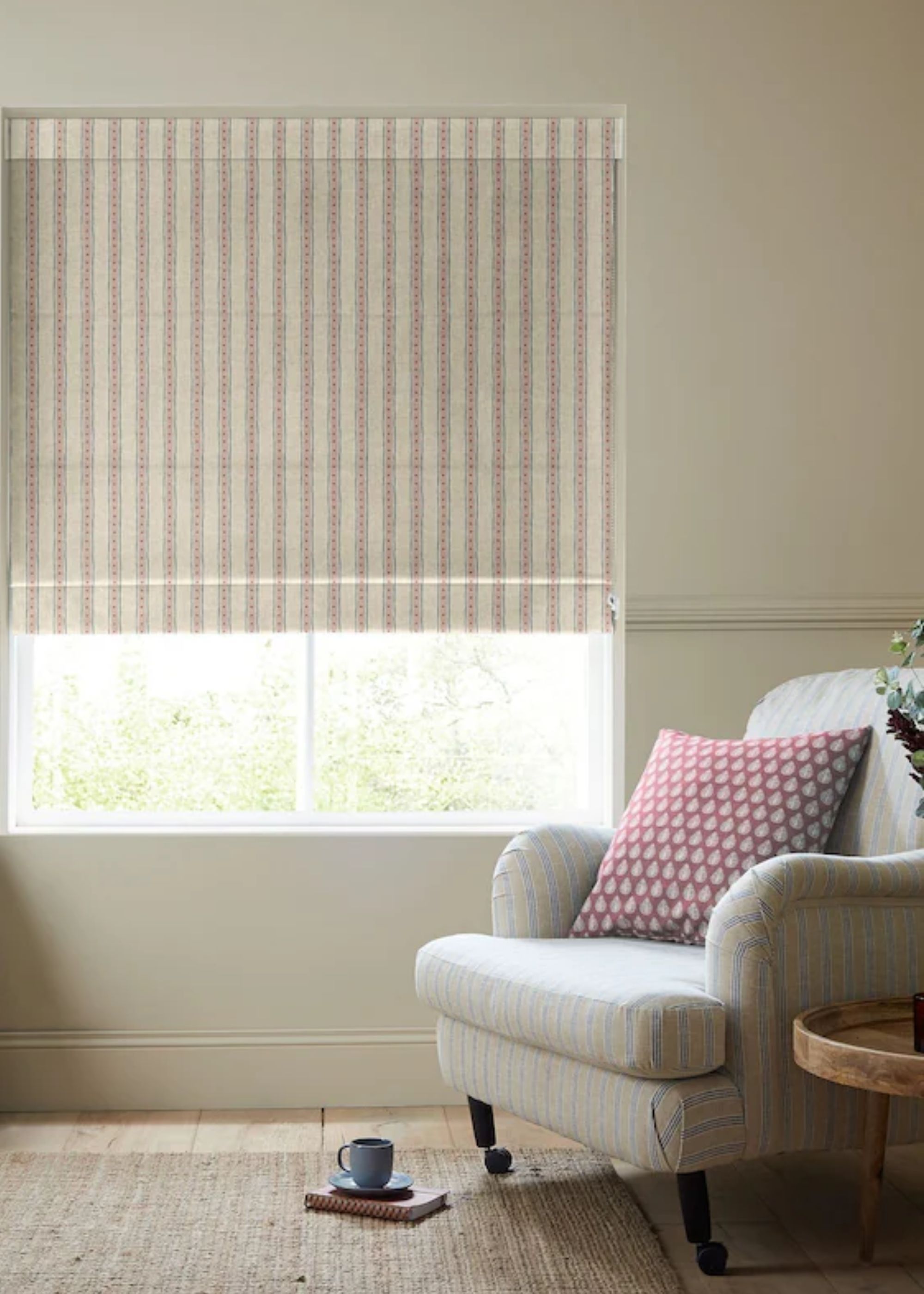 An accent chair with a red and white pillow on top. There are also striped blinds in the living room area