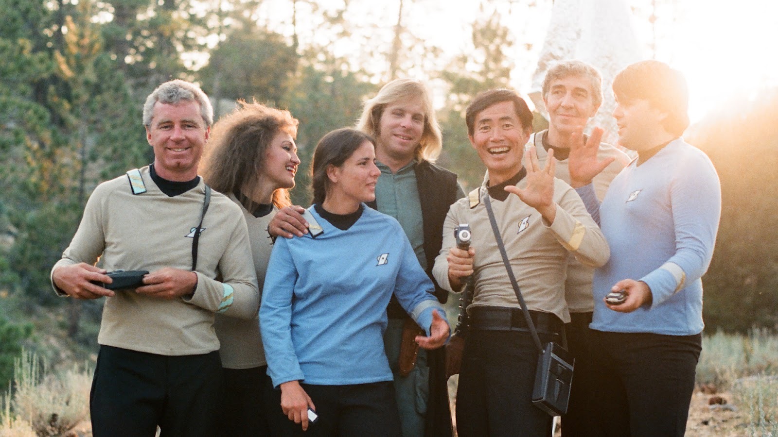 a group of people smiling in a field wearing star trek uniforms including george takei as hikaru Sulu in a still from the documentary beam me up sulu