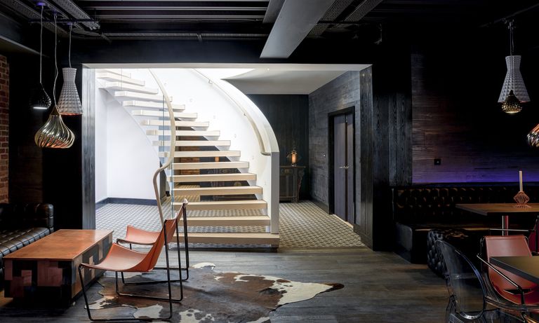 Helical staircase leading to basement with dark wood and brick walls and seating area and dining table