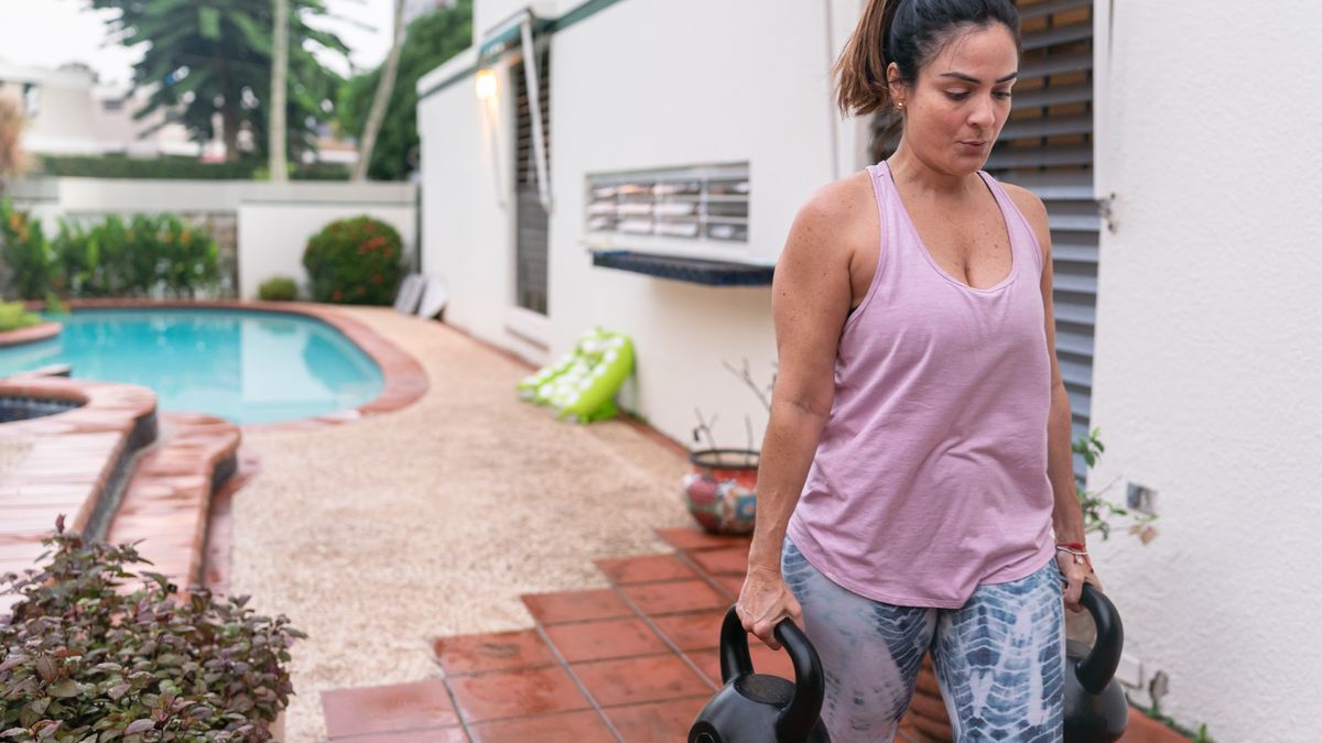 Woman performing the farmer&#039;s walk loaded carry outside using kettlebells