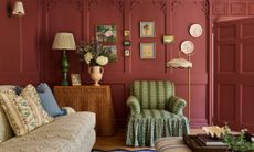 a red pink painted drawing room with historic wall paneling and moldings, skirted furniture, tiny art and a patterned sofa