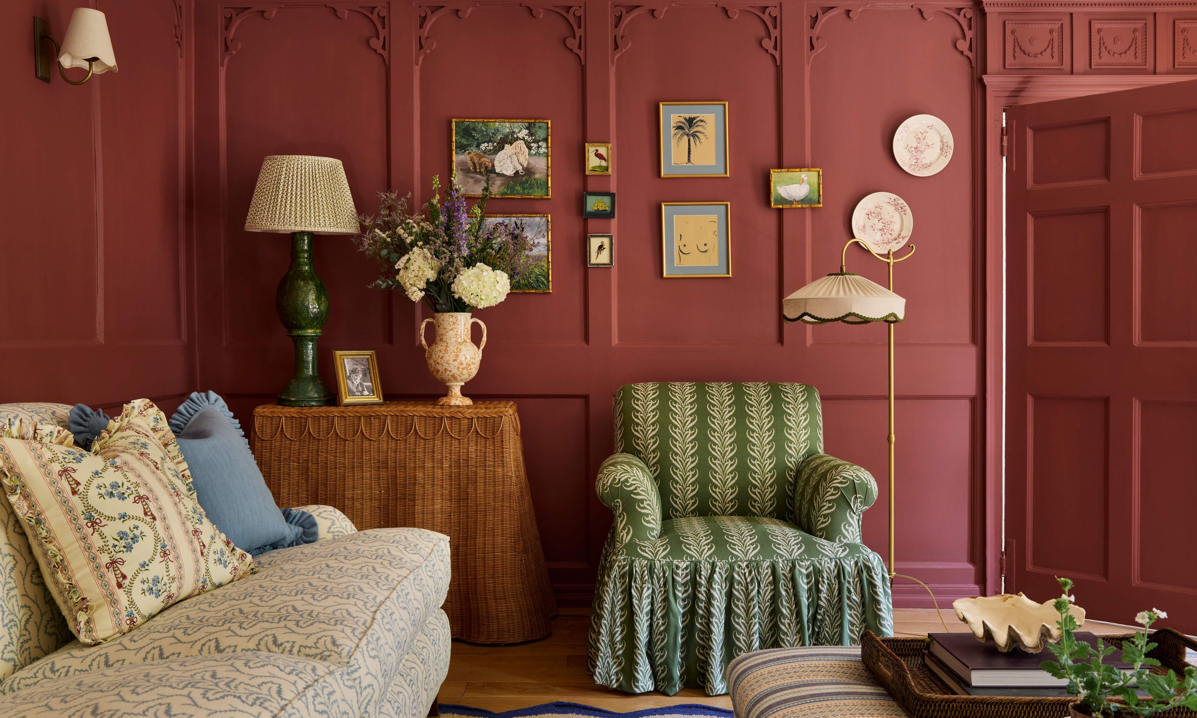 a red pink painted drawing room with historic wall paneling and moldings, skirted furniture, tiny art and a patterned sofa