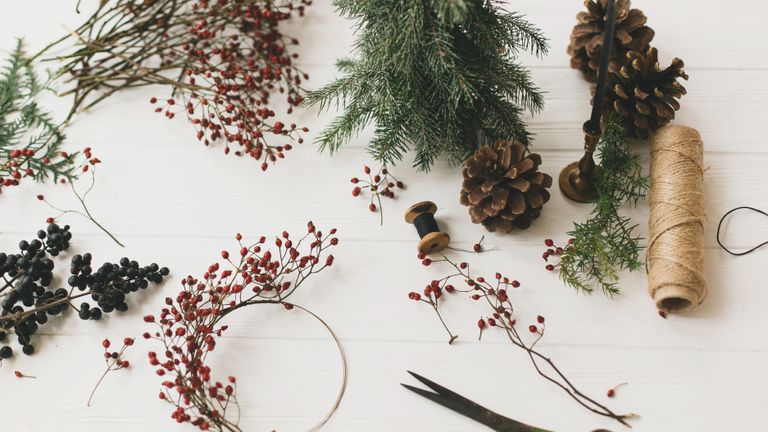 a tablescape of a person creating DIY Christmas wreath with berries, foliage and tools