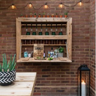 outdoor space with wooden table and wooden crate shelving, fairy lights on an exposed brick wall and a white candle