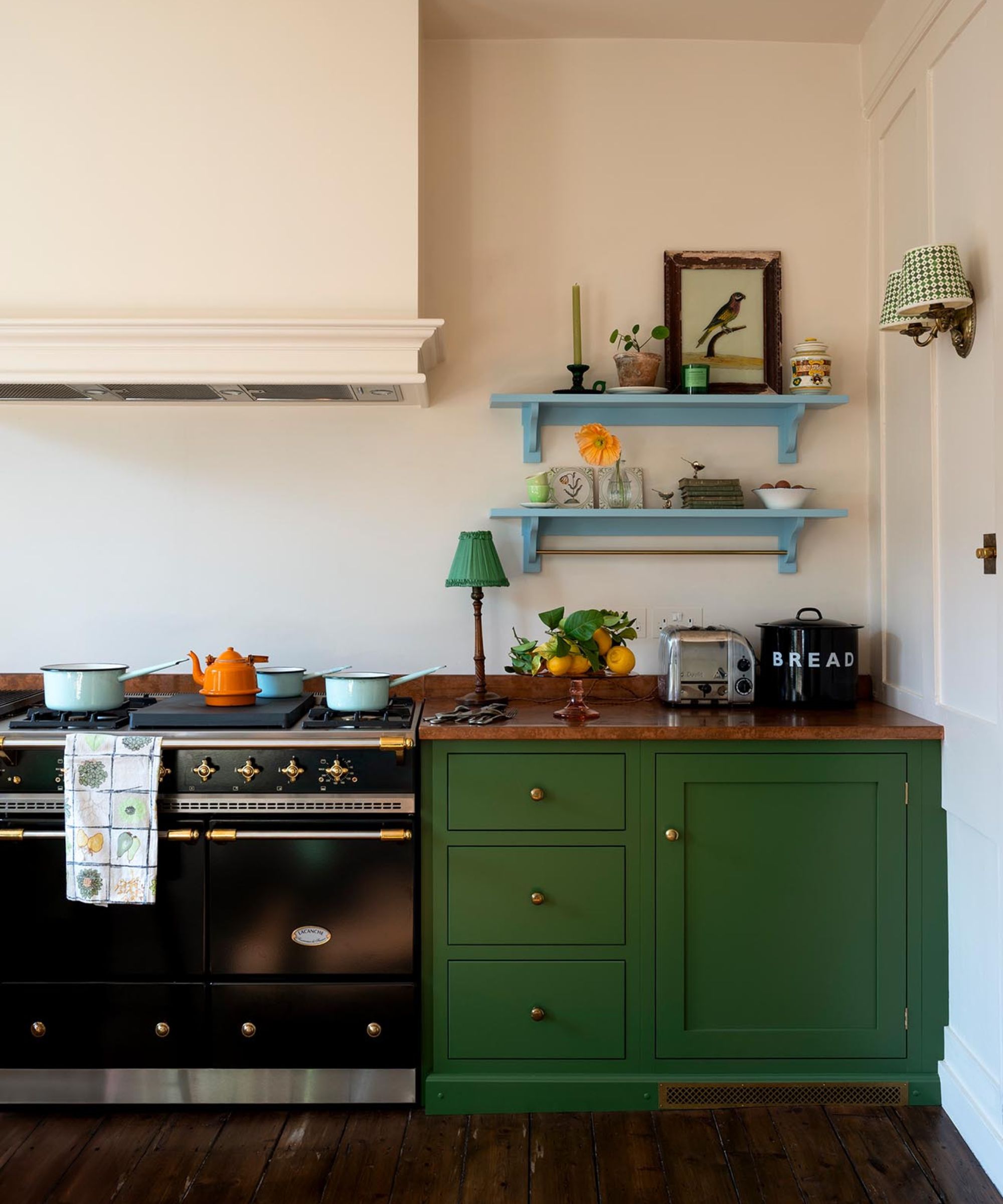A small green kitchen with copper countertops and two blue floating shelves filled with vintage decor