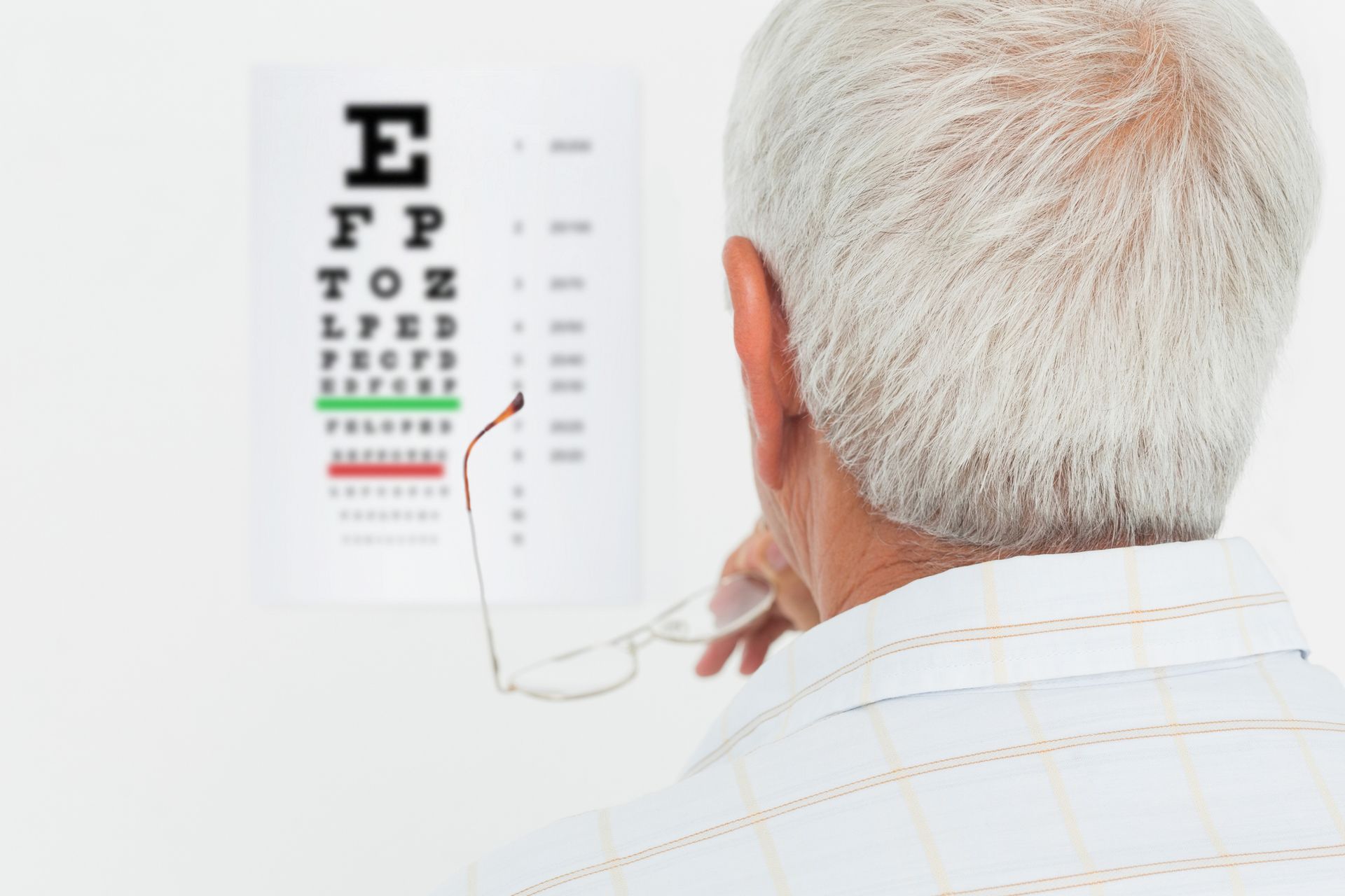 Close-up rear view of a senior man looking at eye chart at medical office
