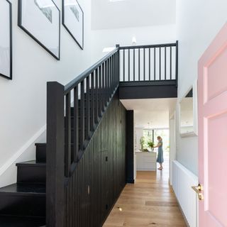 Monochrome hallway with white walls, black staircase and pink door