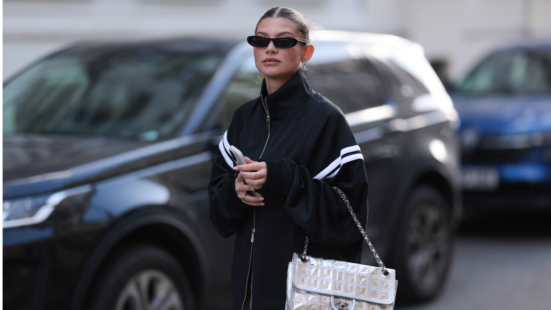 Woman wearing a track jacket and carrying a white shoulder bag with black sunglasses 