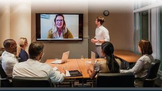 Image of a meeting room with colleagues all facing a video screen with a remote colleague