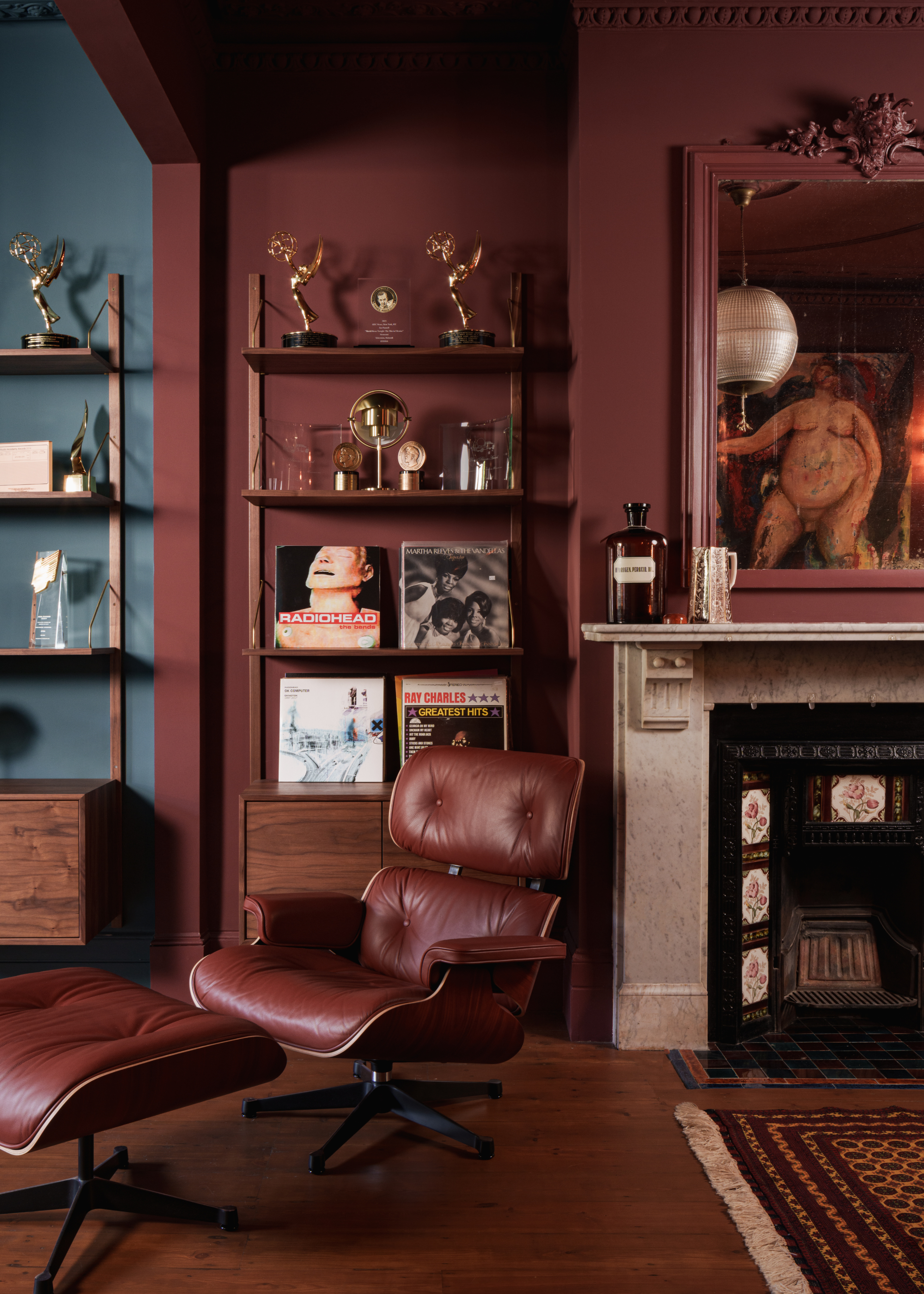 Rooms zoned with color, with one section of the room painted in teal and the other a rust brown-red with a fireplace, open shelving, and an accent chair