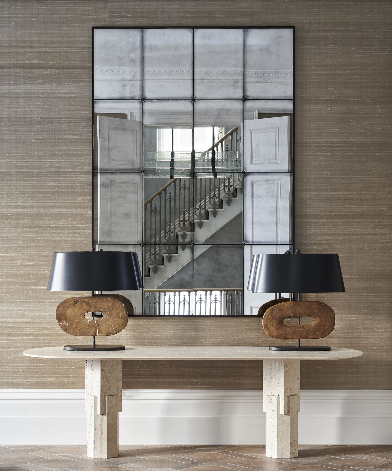 A hallway lighting idea with two contemporary table lamps on a console table, with large mirror behind