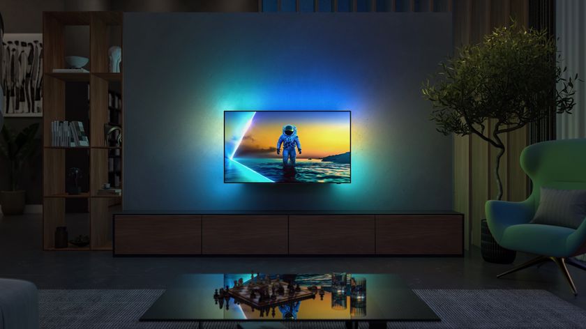 A Philips OLED810 TV wall-mounted in a high-end lounge. On screen is an astronaut on a planet, with Ambilight spilling the same-coloured light onto the wall behind it.