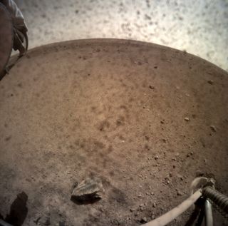 NASA’s InSight lander flipped open the lens cover on its Instrument Context Camera (ICC) on Nov. 30, 2018, and captured this view of Mars. Located below InSight’s deck, the ICC has a fisheye view, creating a curved horizon. Some clumps of dust are still visible on the camera’s lens. One of the spacecraft’s footpads can be seen in the lower right corner. The seismometer’s tether box is in the upper left corner.