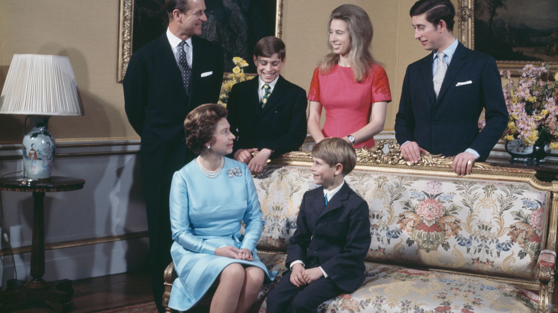 The Royal Family sit and stand around a sofa