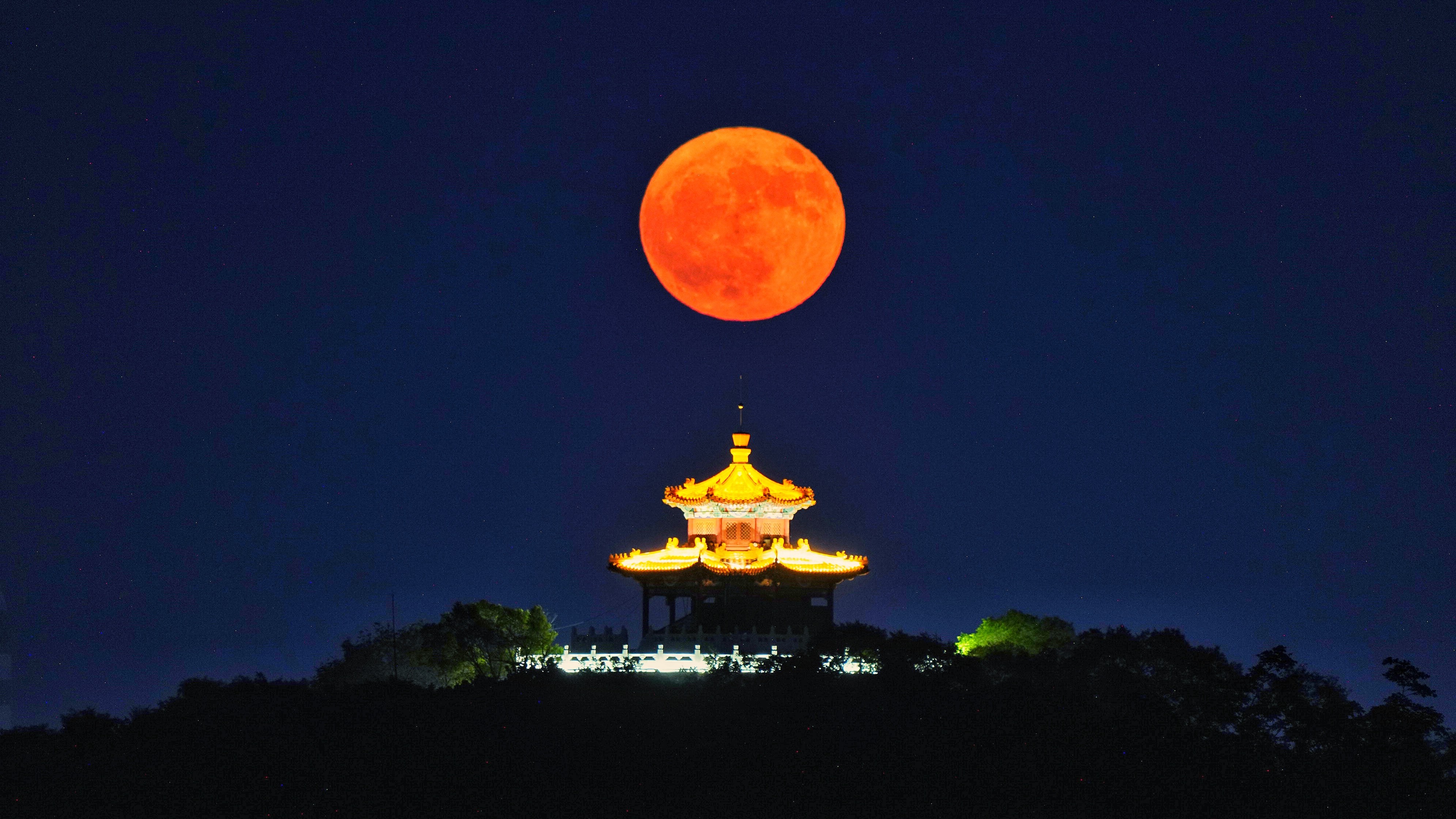a red strawberry moon hangs low in the sky above an ornate building