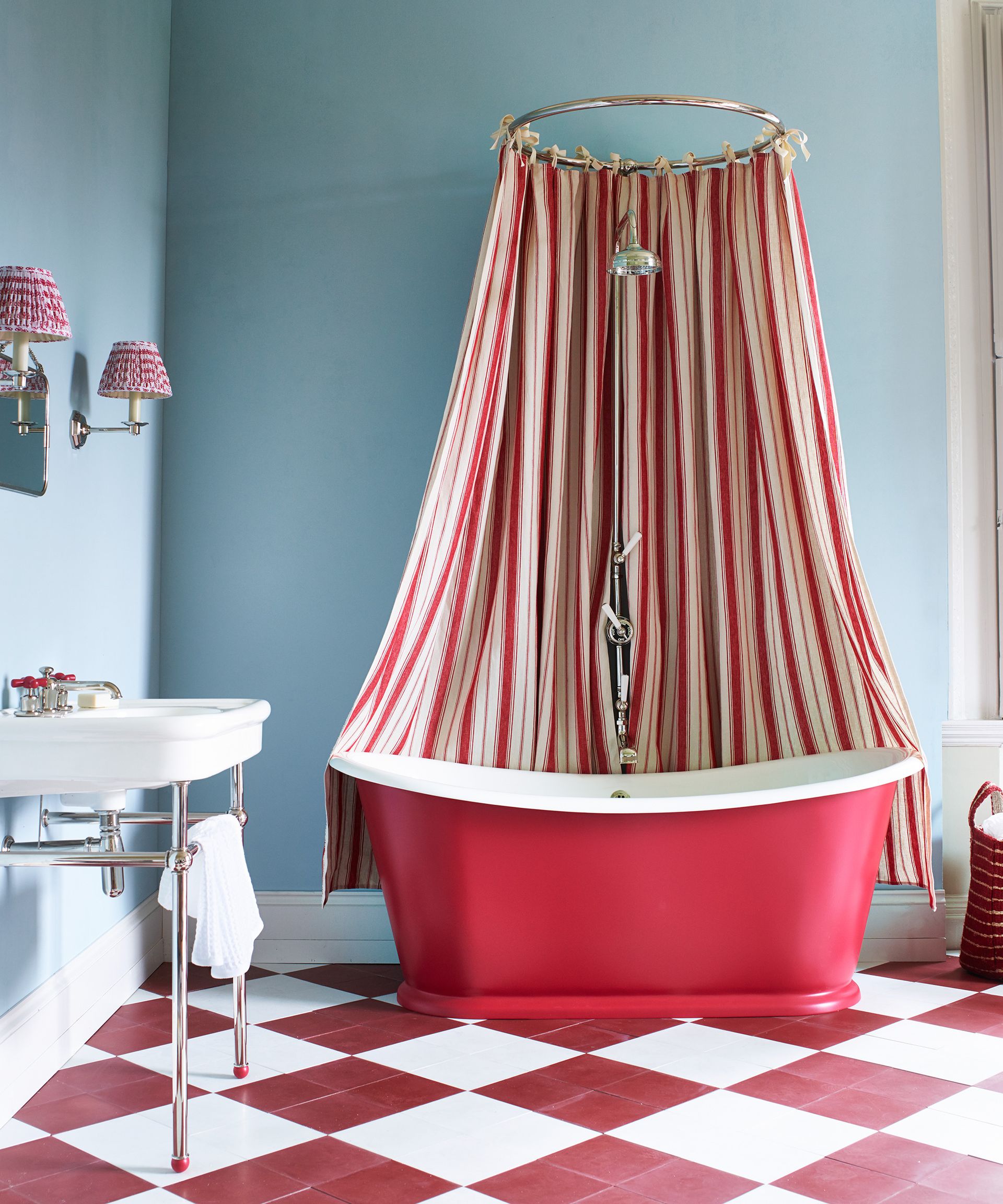 A red roll top bath in front of a light blue wall sat on a red and white checkered floor