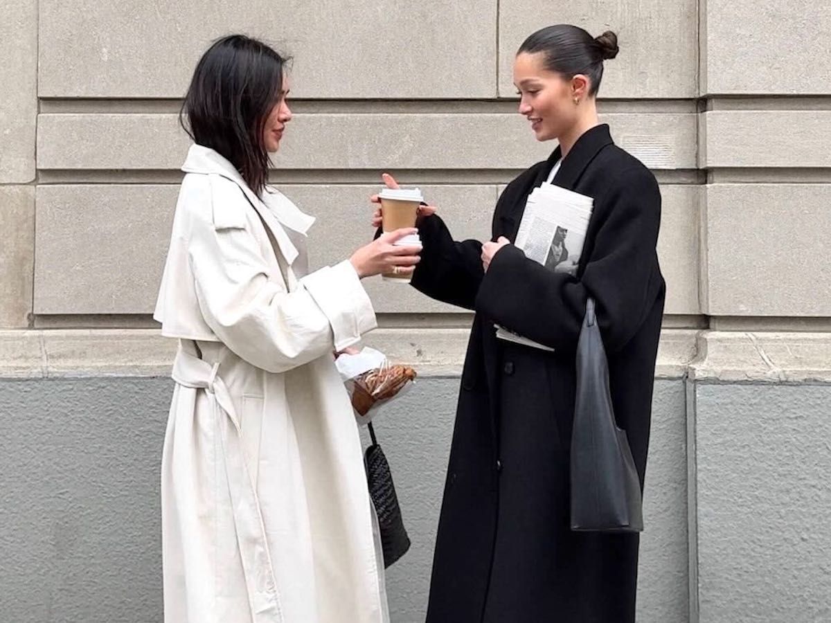 style influencer Mimi Nguyen poses with a friend on a NYC sidewalk holding coffees and wearing chic spring outfits with maxi trench coats and leather bags