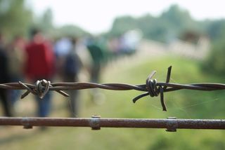 barbed wire with migrants in the background.