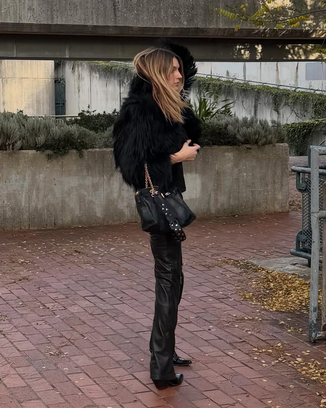 A woman wearing a black faux fur jacket, boots, and black pants.