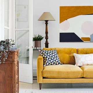 White living room with large brass table lamp behind mustard sofa