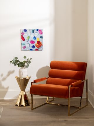 A living space with a red chair, a gold side table, and art on the wall