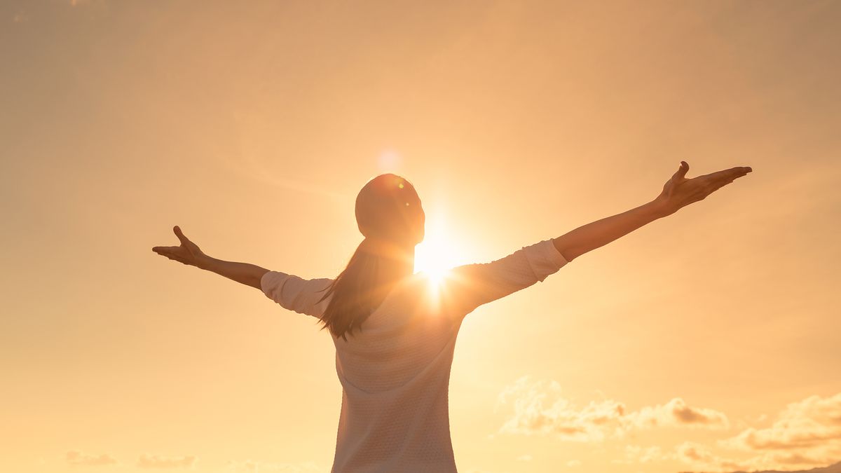 A woman standing in the sun with her arms outstretched and palms lifted up