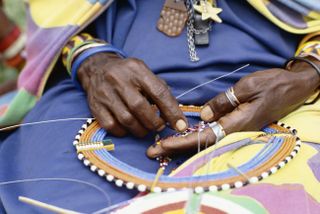 A closeup of a Kenyan woman's hands as she puts colorful beads on a string