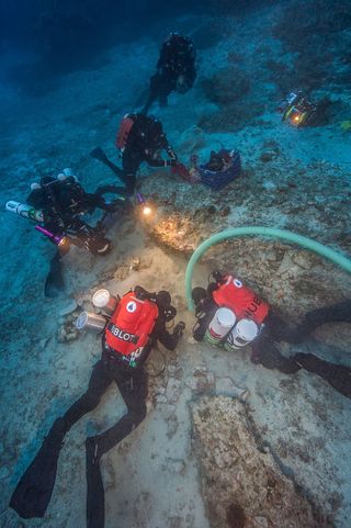 Archaeologists use a water dredge and submersible pump 180 feet (55 meters) below the ocean surface at the Antikythera shipwreck site. Ten archaeologists performed 61 dives over 10 days in 2015, using closed-circuit rebreathers and trimix breathing gases.