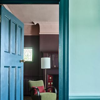 An open blue-painted door open to a living room with dark purple walls and a soft pink-painted ceiling