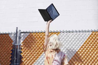 Young woman holds up Google Pixelbook Go next to chainlink fence.