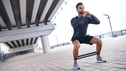 Man doing resistance band squat outside