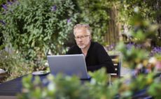 An older man concentrates on his laptop screen while checking 401(k) fees outdoors.
