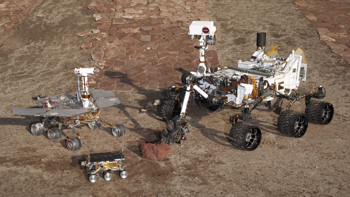 Three generations of NASA Mars rovers on display at the Jet Propulsion Laboratory in California: a model of the twin Spirit and Opportunity rovers on the left, the Sojourner rover&#039;s ground twin below, and a model of the Mars Curiosity rover on the right.