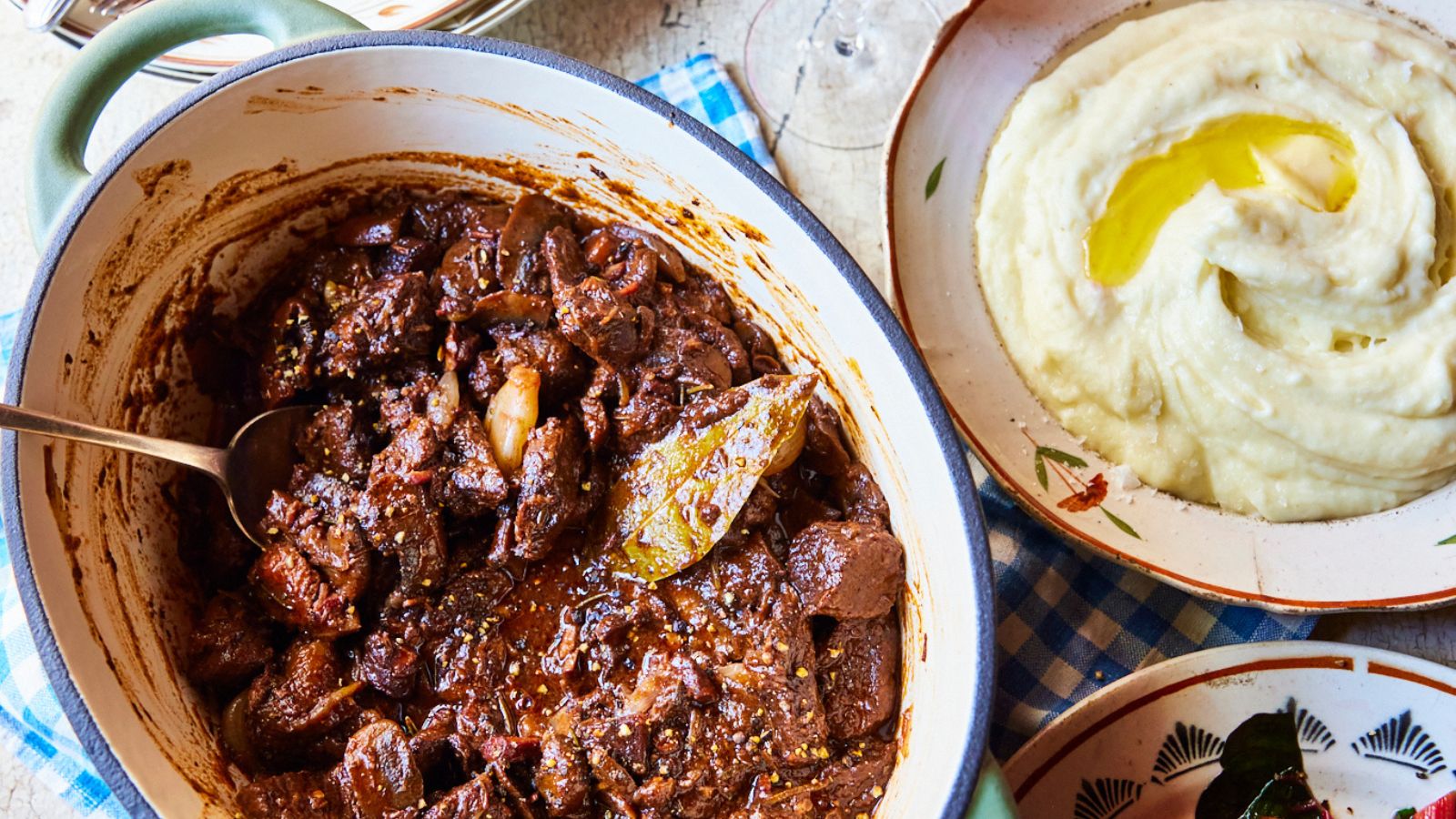 dutch oven with beef bourguinon and a dish of mashed potato next to it