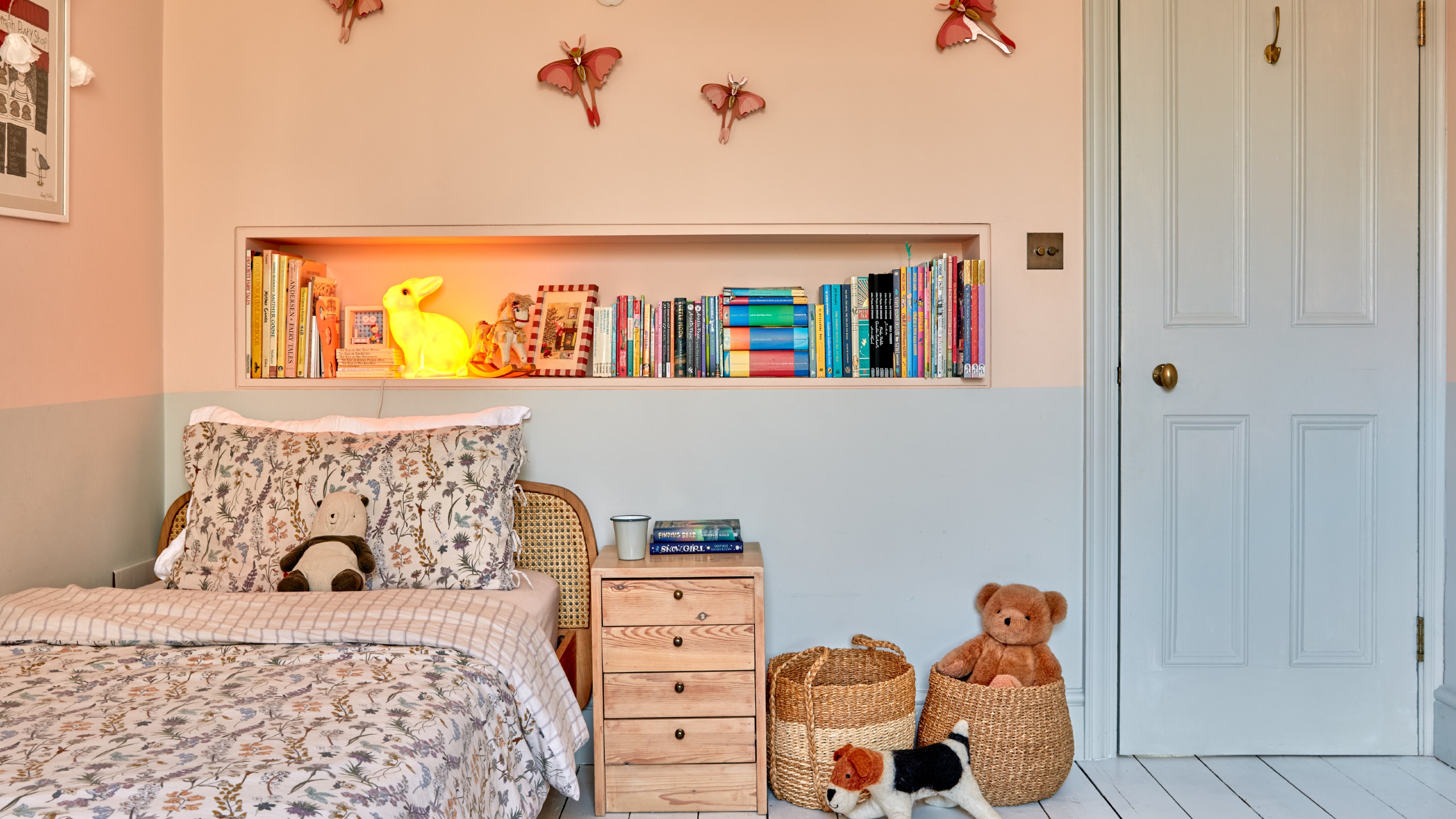 A girl's bedroom with two-tone walls in pink and grey with butterfly decor on the wals and a rattan bed