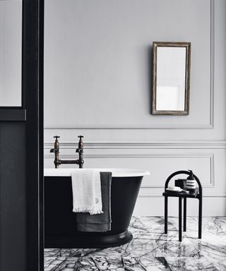 A smart black bathtub with aged brass faucets sits on a marble bathroom floor