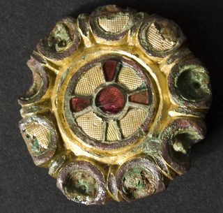 this brooch contains gold textured in a waffle shape along with a cross made of red glass and semiprecious stone