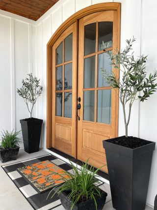 A wooden front door with two planters and a floral orange patterned doormat