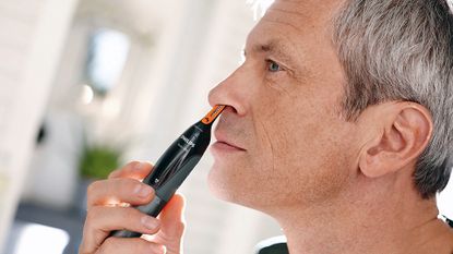 A man, looking in the mirror, trimming his nose hair with one of the best nose hair trimmers from Philips